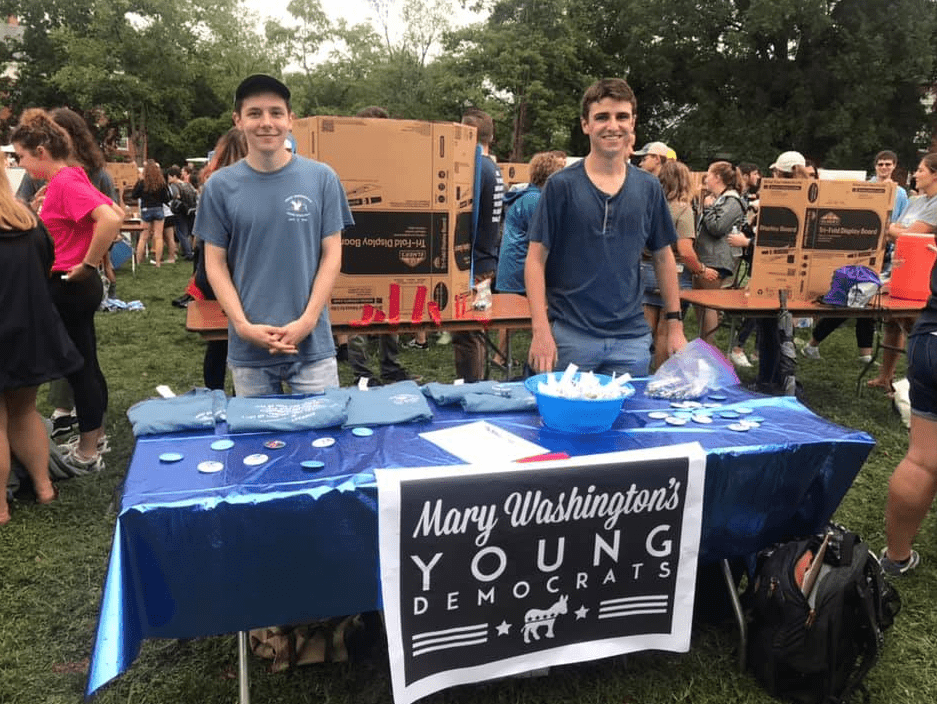 Sam Hartz and Patrick Healy stand behind a table with a sign that says Mary Washington's Young Democrats.