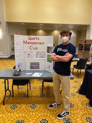 A blonde guy standing next to a fold out board that says "Sports Management." He is smiling.