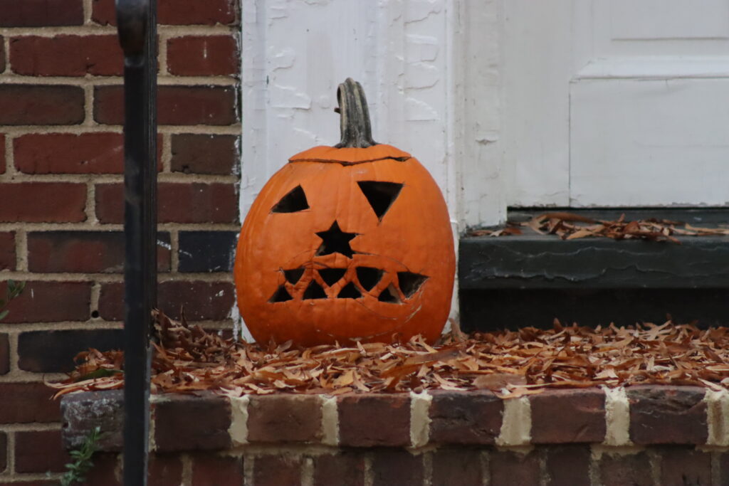 A carved pumpkin sitting on a doorstep. The eyes are triangle, the nose is a star, and the mouth is made of triangle teeth.