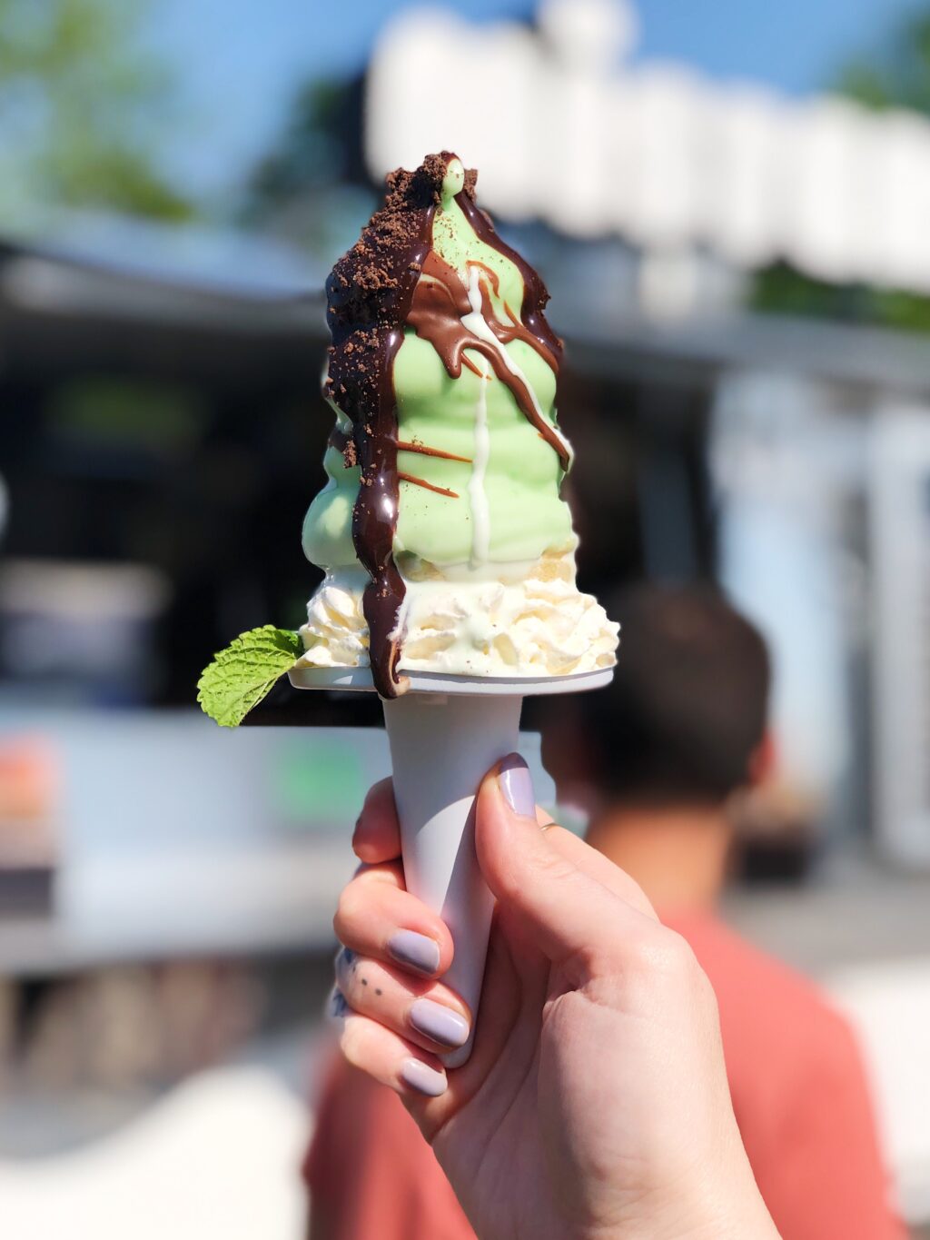 A paper cone of mint ice cream, drizzled with chocolate.