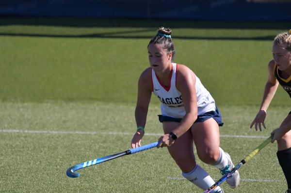 A female field hockey player leans forward with her tool to grab the ball.