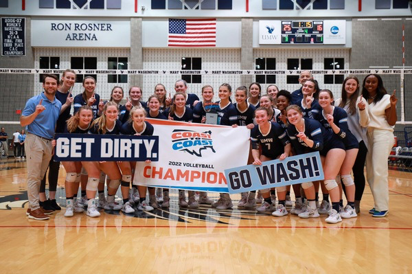 A group of students in navy blue volleyball uniforms pose together. They are holding signs that say "Get Dirty," "Go Wash," and "Coast to Coast 2022 Volleyball Champion"