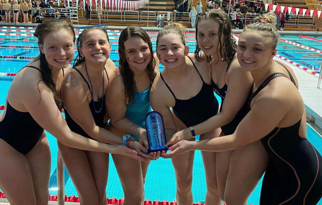 A group of six female swimmers hold a trophy.
