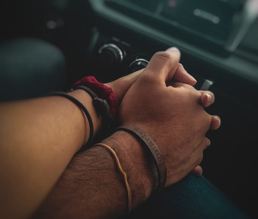 Two people hold hands over the center console in a car.