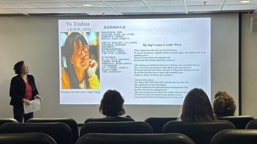 A Chinese woman stands in front of a slideshow introducing Chinese poet Yu Xiuhua.