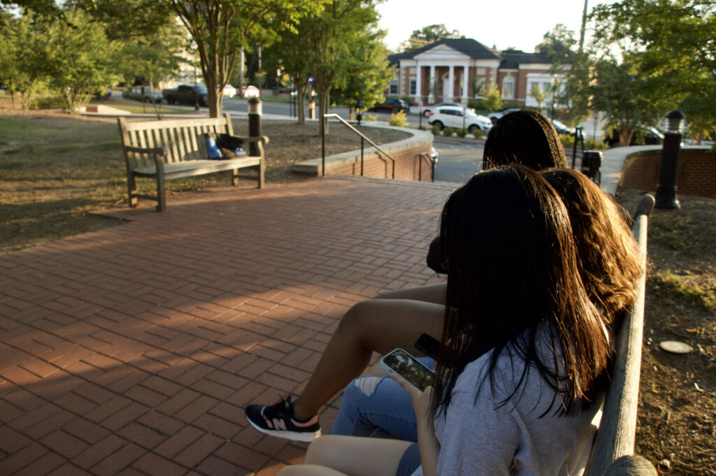 Three girls sitting on the bench watching TikTok on their phones