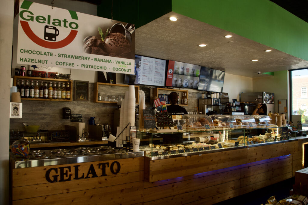 Glass front counter with a variety of pastries on display with a gelato station off to the right hand side of the counter. Workers are operating the front counter.