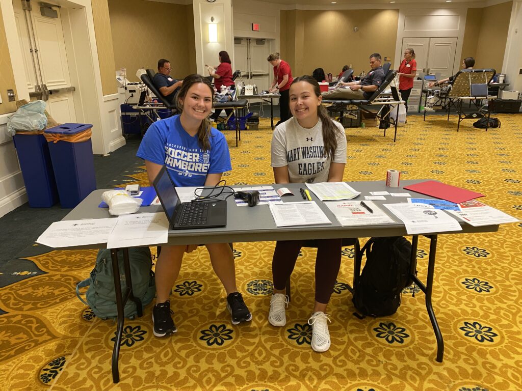 Madison Mayes and Sabrina Perez smiling while sitting behind the check in table during the Red Cross Blood Drive