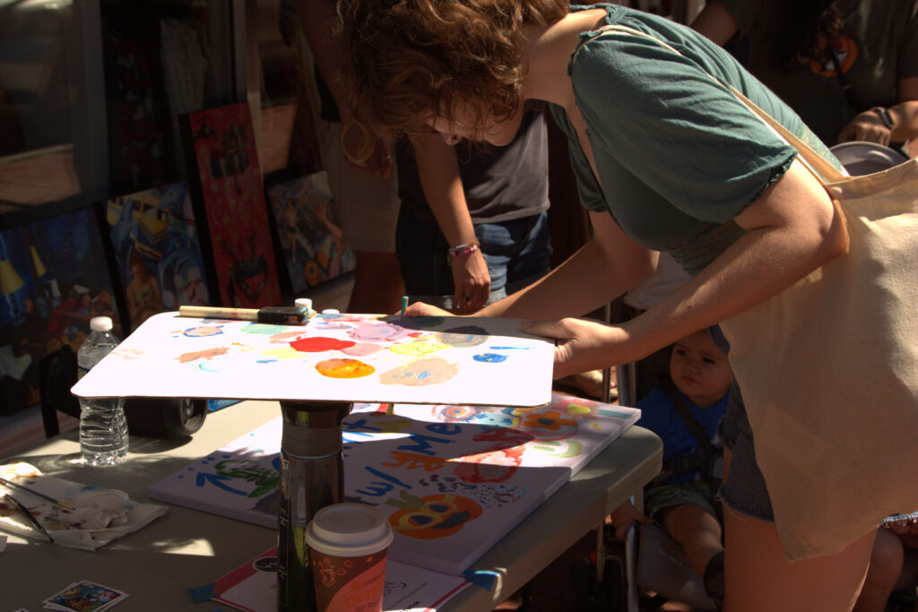 Busy street with artists on the sidewalk painting and displaying their artwork for others to see.