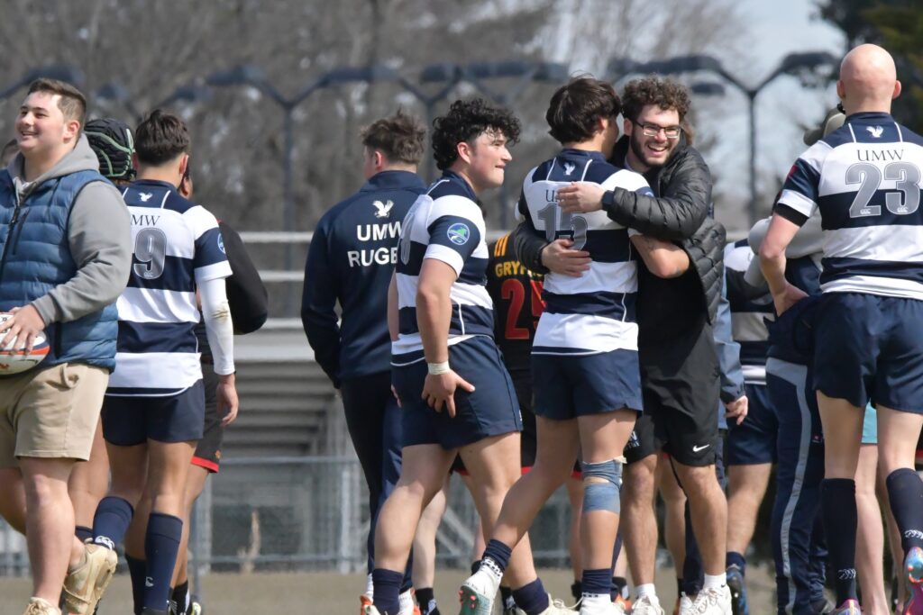 Photo of a group of rugby men playing and hugging each other on the field during a game