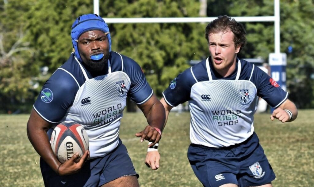 Two mens rugby players, including Daniel Bullock who holds the ball, run side-by-side down the field.