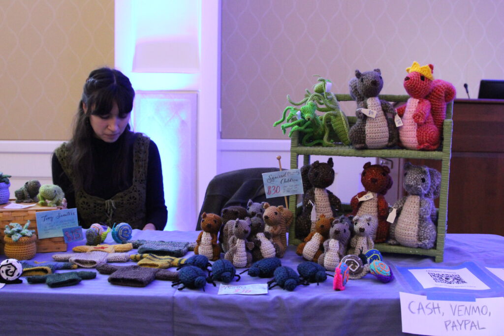 Megan Cena sits behind her table while selling her crochet items such as squirrels, snails, and more.