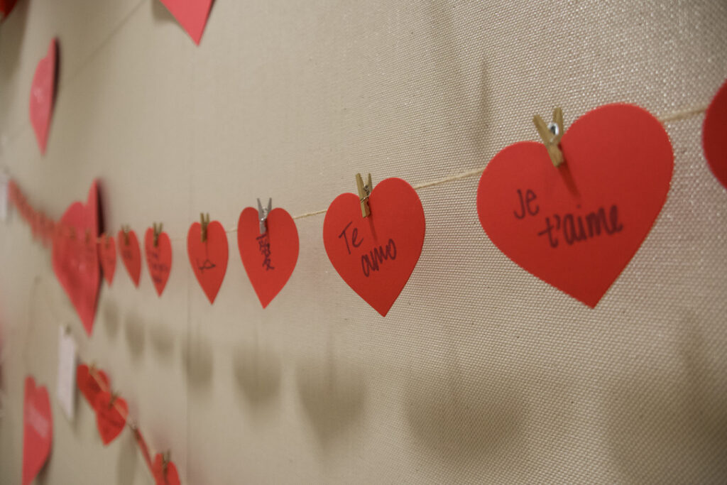 Three paper hearts hung on a clothesline with different languages written on them, universally meaning "I love you."