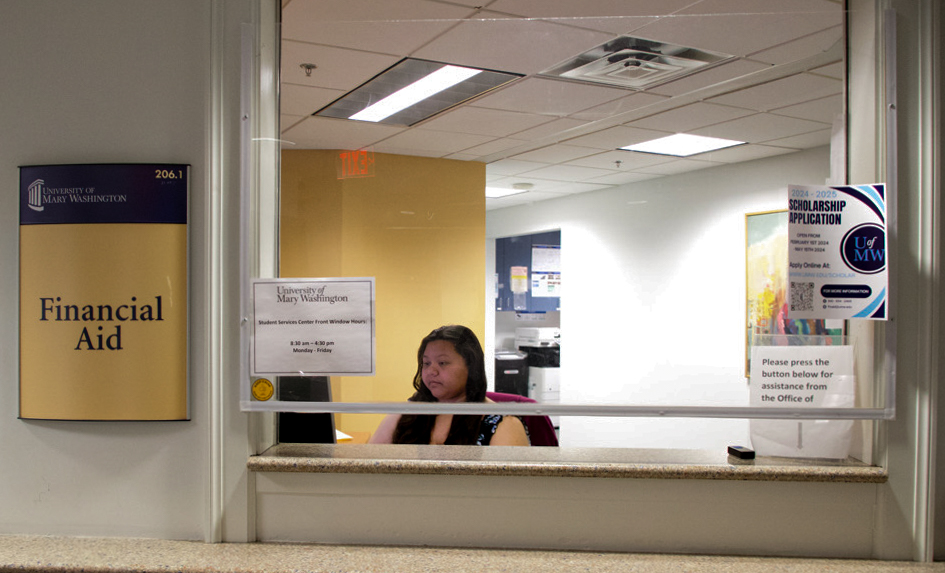 A lady working and using her computer behind the "Financial Aid" sign.