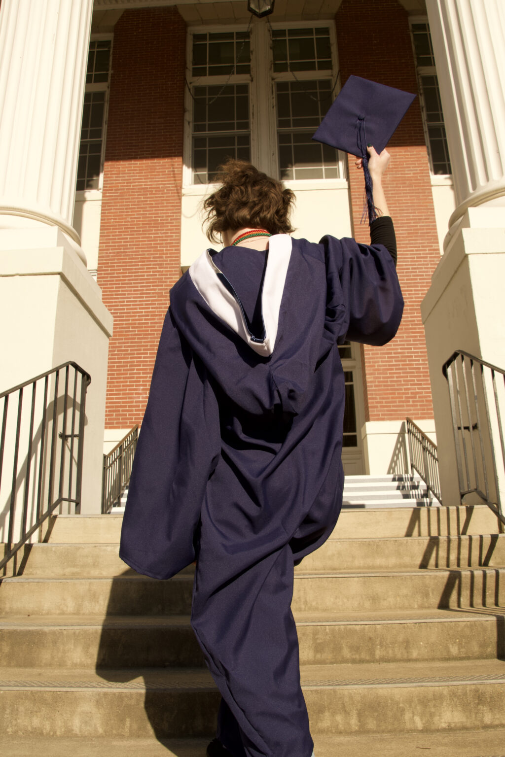 Student dressed in graduation regalia going up steps.