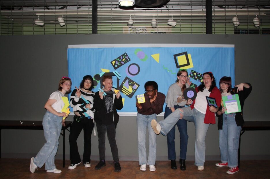A group of seven students happy and posing with cut-out designs.