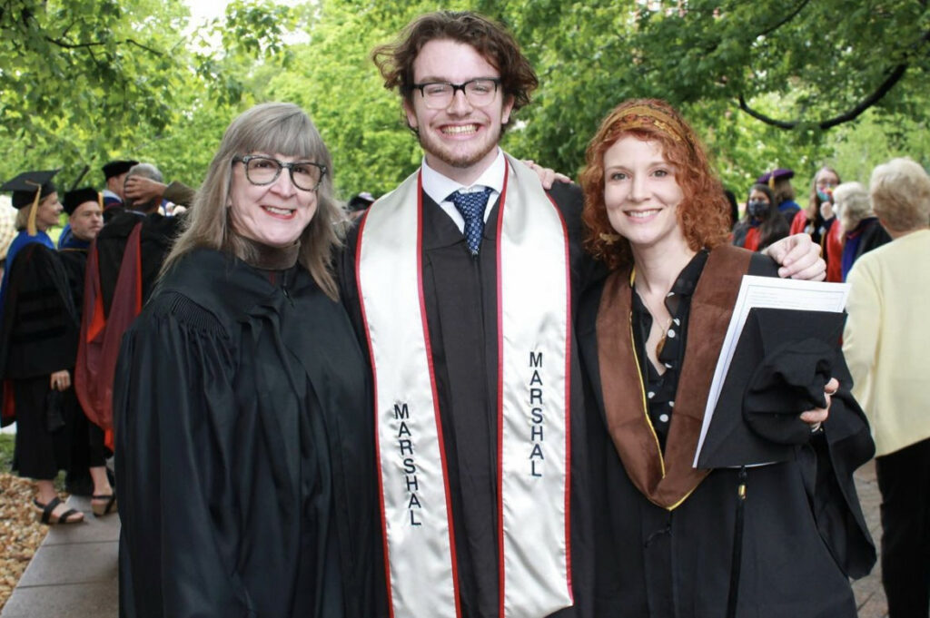 Joseph Selding smiling at graduation next to two other faculty members