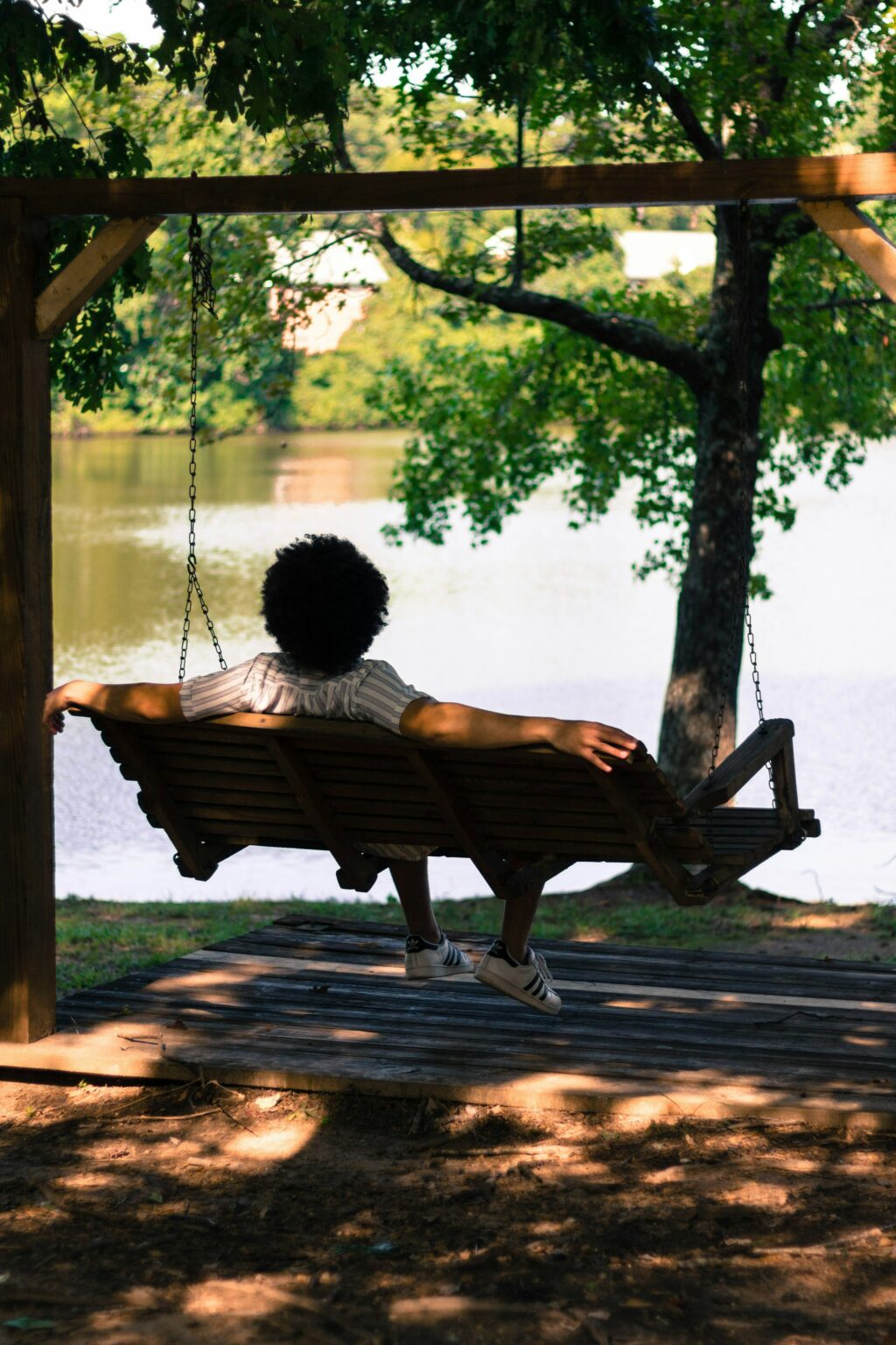 Man on a hanging bench looking at a lake enjoying the view.