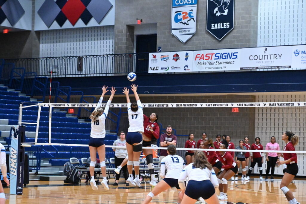 Two University of Mary Washington players jump up at the net to try to block the ball as a Virginia Union University player tries to spike it.