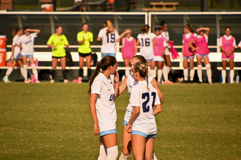 A group of three University of Mary Washington players circle around each other talking during a game break.