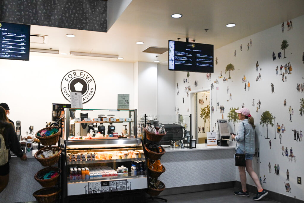 A photo of a coffee shops main counter with food out. A customer is seen picking up their order.