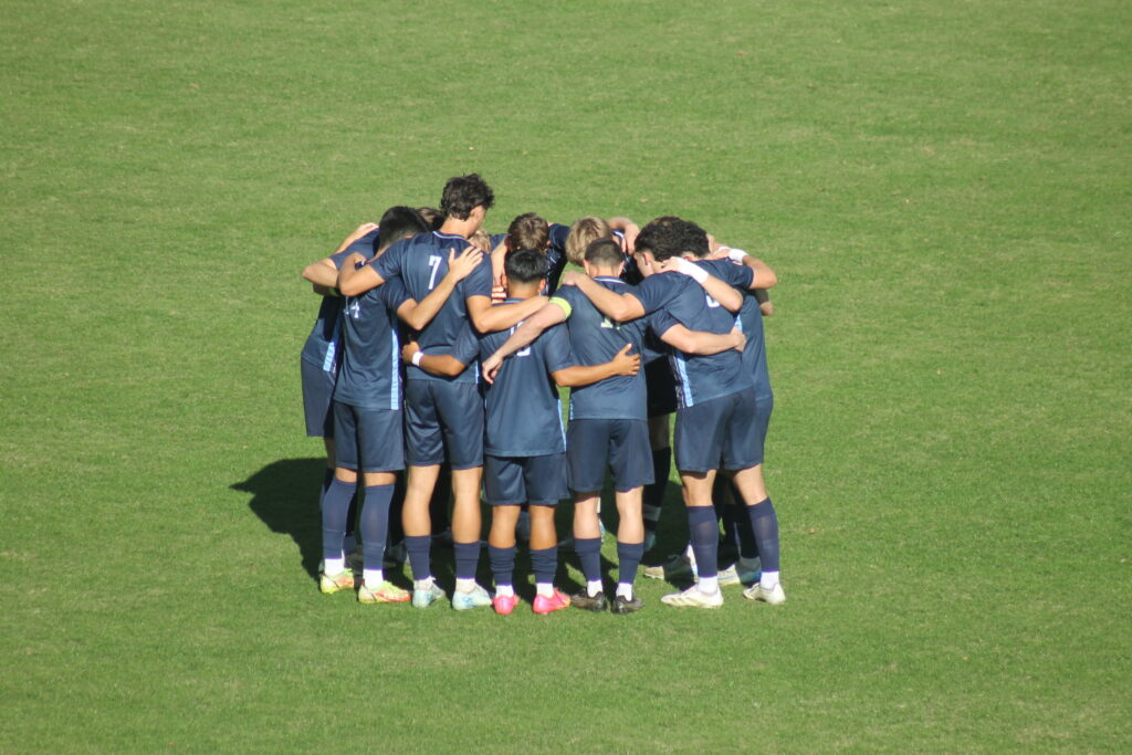 The men's soccer team huddled in a group on the field.