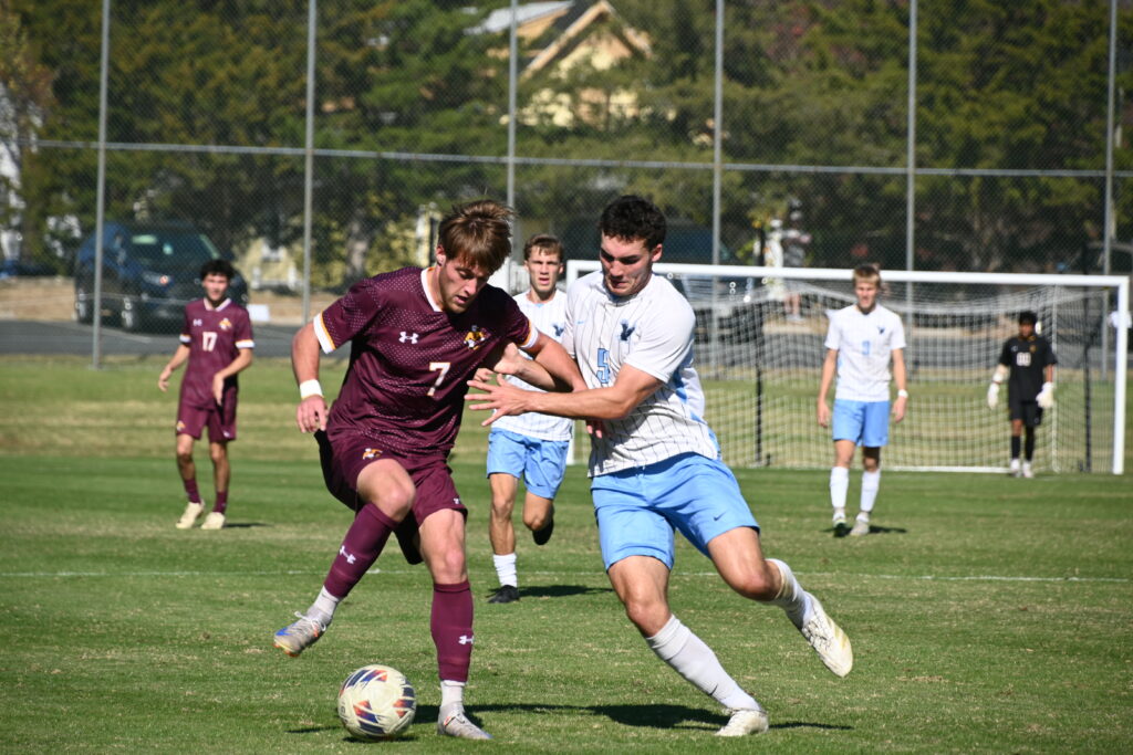 A University of Mary Washington soccer player leans into a Salisbury University player who has the ball. Both UMW and Salisbury players are behind the two players with their fronts to the camera.